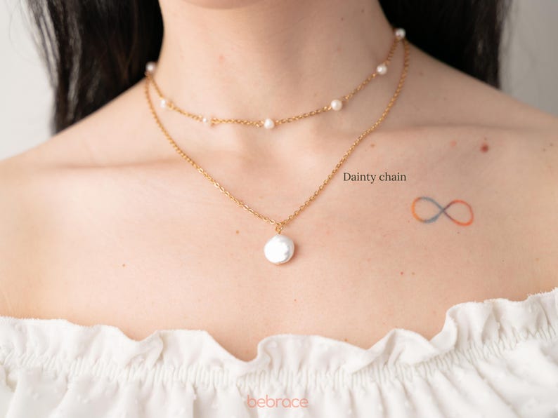 Op de afbeelding: Een gouden ketting met een grote parel hanger en een kleinere parelketting eroverheen gelegd. De tekst "Dainty chain" staat op de afbeelding.