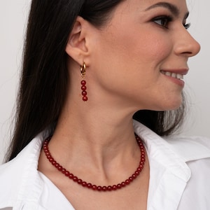 May include: A red carnelian necklace and earrings set. The necklace is made of small, round beads and the earrings are dangle style with four beads.