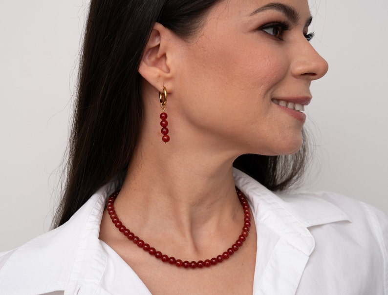 May include: A red carnelian necklace and earrings set. The necklace is made of small, round beads and the earrings are dangle style with four beads.