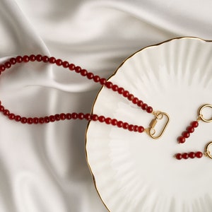 May include: A red carnelian beaded necklace with a gold clasp and matching red carnelian beaded earrings with gold hoops.