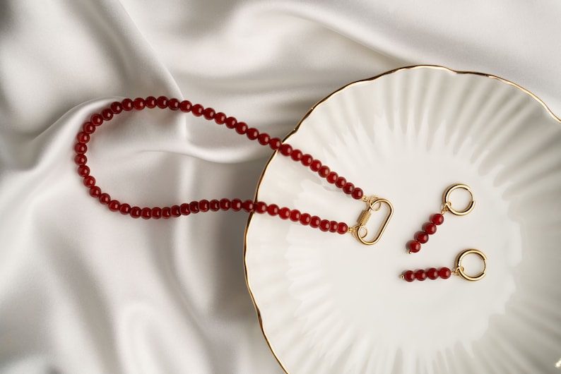 May include: A red carnelian beaded necklace with a gold clasp and matching red carnelian beaded earrings with gold hoops.