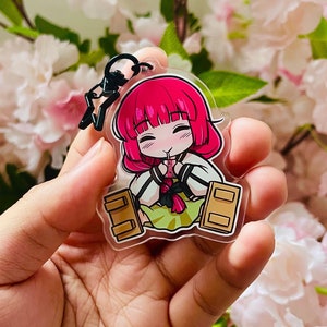 Puede incluir: Un llavero acrílico transparente con un personaje de dibujos animados con cabello rosado y un atuendo blanco y verde. El llavero tiene un cierre negro y un anillo de metal negro para sujetarlo. El personaje está sonriendo y sosteniendo una bebida.