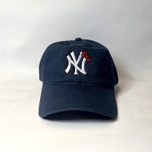 Könnte beinhalten: Eine marineblaue Baseballkappe mit einem weißen gestickten New York Yankees Logo und einer roten Hello Kitty Schleife.