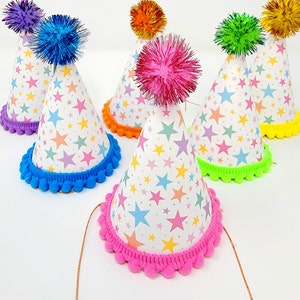 May include: A set of six colorful party hats with star patterns and pom-poms. The hats are in various colors, including purple, blue, orange, green, and pink.