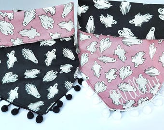 May include: Two triangular pet bandanas featuring a ghost pattern. One bandana is black with white ghosts and black pom-pom trim. The other is pink with white ghosts, white pom-pom trim, and the name Willow embroidered in white script.
