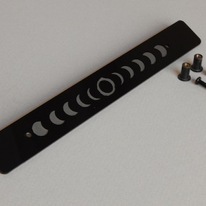 May include: Black metal moon phase wall decor with eight different moon phases etched into the surface. The decor comes with four black screws and four silver washers.
