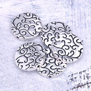 May include: Five silver-toned round metal beads with a decorative swirl pattern.