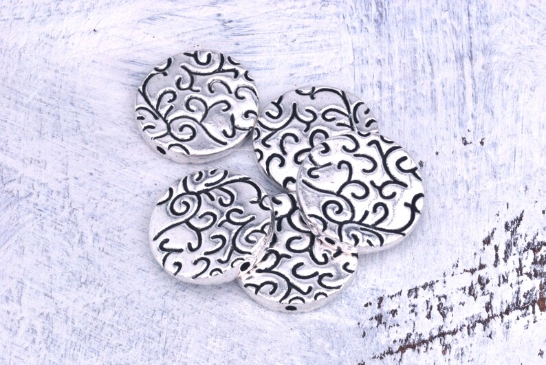 May include: Five silver-toned round metal beads with a decorative swirl pattern.