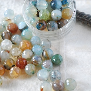 May include: A bowl filled with agate beads in various shades of blue, green, brown, and white. The beads are round and have a smooth, polished finish.