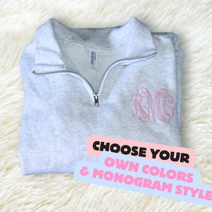 May include: Gray quarter-zip sweatshirt with a pink monogram "RMG" embroidered on the front. The text "CHOOSE YOUR OWN COLORS & MONOGRAM STYLE" is on a pink and blue background.