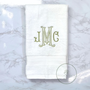 May include: White hand towel with a green embroidered monogram "JMC" on a white marble background.