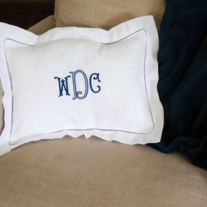 May include: White pillow with a blue embroidered monogram "WDC" on a beige armchair.