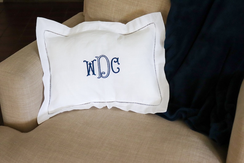 May include: White pillow with a blue embroidered monogram "WDC" on a beige armchair.