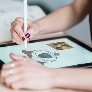 Peut inclure: Une personne utilise un stylet pour dessiner un carlin de dessin animé sur une tablette numérique. Le carlin est brun et blanc et a un cœur au-dessus de sa tête. Une photo d'un carlin est en arrière-plan.