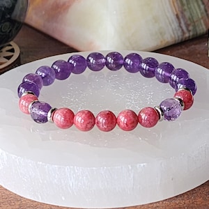 May include: A purple and pink gemstone bracelet with silver beads. The bracelet is made with amethyst and rhodochrosite beads.
