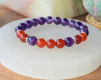 May include: A beaded stretch bracelet featuring alternating round polished purple amethyst and vibrant orange carnelian gemstone beads, accented with small silver-toned metal spacers arranged in a circular pattern on a white surface.