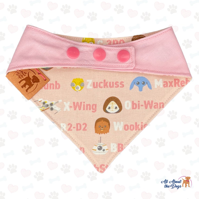 May include: Pink dog bandana with a light pink top section and three pink buttons. The bandana features Star Wars characters and text including "X-Wing", "Obi-Wan", and "Wookie". The tag reads "All About the Dogs".