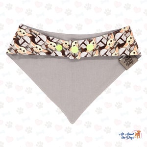 May include: A grey dog bandana with a brown and yellow pattern of a popular character from a science fiction film. The bandana has two yellow buttons and a brown tag that says "All About the Dogs".