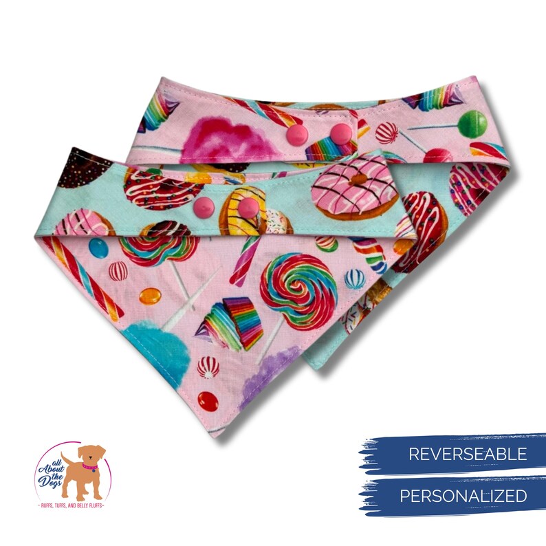 Pu&ograve; includere: Bandana reversibile per cani a tema caramelle. La bandana presenta lati rosa e verde acqua, ciascuno ricoperto da illustrazioni colorate di lecca lecca, ciambelle e altri dolci. La bandana ha chiusure a scatto rosa. Il testo "REVERSEABLE" e "PERSONALIZED" &egrave; sull'immagine.