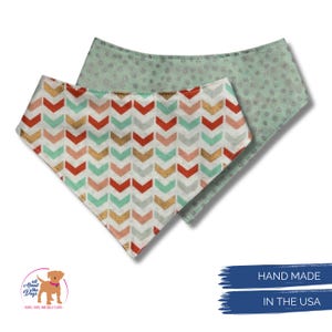 May include: Two dog bandanas. One features a chevron pattern in red, gold, mint, and peach. The other is mint green with a small dot pattern. The bandanas are handmade in the USA.