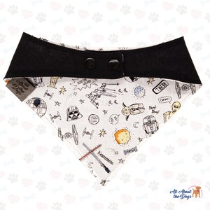 Op de afbeelding: Een witte hondenbandana met een zwarte rand en een Star Wars-thema. De bandana heeft verschillende Star Wars-personages en -symbolen, waaronder Darth Vader, R2-D2 en de Millennium Falcon. De bandana heeft een knoopsluiting.