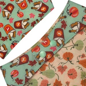 Puede incluir: Bandana para perros con un patr&oacute;n repetido de tazas de caf&eacute;, golosinas de hueso para perros, calabazas y hojas de arce sobre un fondo turquesa. La bandana tiene dos botones verde claro. El otro lado tiene un patr&oacute;n de calabazas y hojas.