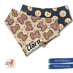 May include: Two reversible dog bandanas. One is cream-colored with red and white striped bone shapes and the name "Elora". The other is navy blue with snowman cookie designs. The bandanas are personalized.