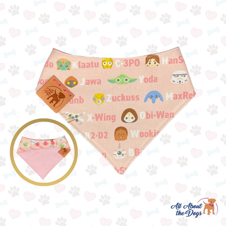 May include: A pink dog bandana featuring Star Wars characters and names. The bandana has a light pink background with character illustrations and names like Yoda and C-3PO. A smaller, folded bandana is shown in the lower left corner.