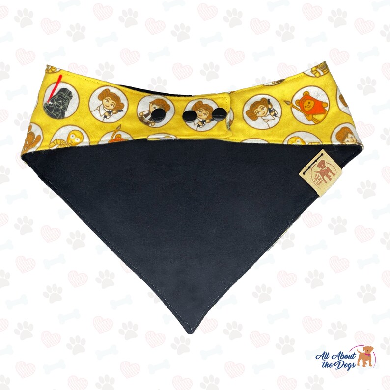 May include: Yellow dog bandana with a Star Wars theme featuring characters like Darth Vader, Princess Leia, and Chewbacca. The bandana has a black underside and a brown leather tag with the text "All About the Dogs".