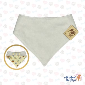 May include: A light grey dog bandana with a brown leather tag that says "All About the Dogs". The bandana has a snap closure and is made of a soft, comfortable fabric.