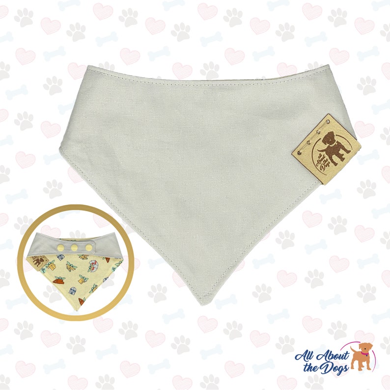May include: A light grey dog bandana with a brown leather tag that says "All About the Dogs". The bandana has a snap closure and is made of a soft, comfortable fabric.