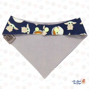 K&ouml;nnte beinhalten: Ein marineblaues Bandana mit einer wei&szlig;en und grauen R&uuml;ckseite. Das Bandana zeigt ein sich wiederholendes Muster eines gr&uuml;nen Alien-Charakters mit einem braunen Satchel. Das Bandana hat drei gelbe Kn&ouml;pfe und ein Etikett mit der Aufschrift "All About the Dogs".