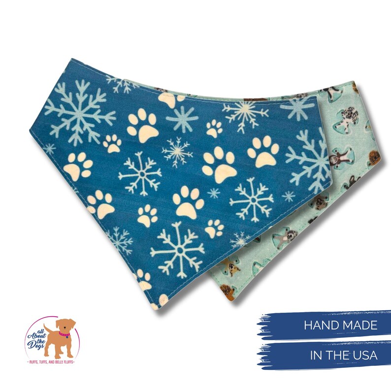 K&ouml;nnte beinhalten: Zwei Hunde-Bandanas. Eines ist blau mit wei&szlig;en Pfotenabdr&uuml;cken und Schneeflocken. Das andere ist hellblau mit Hundeillustrationen. Die Bandanas sind handgefertigt in den USA.