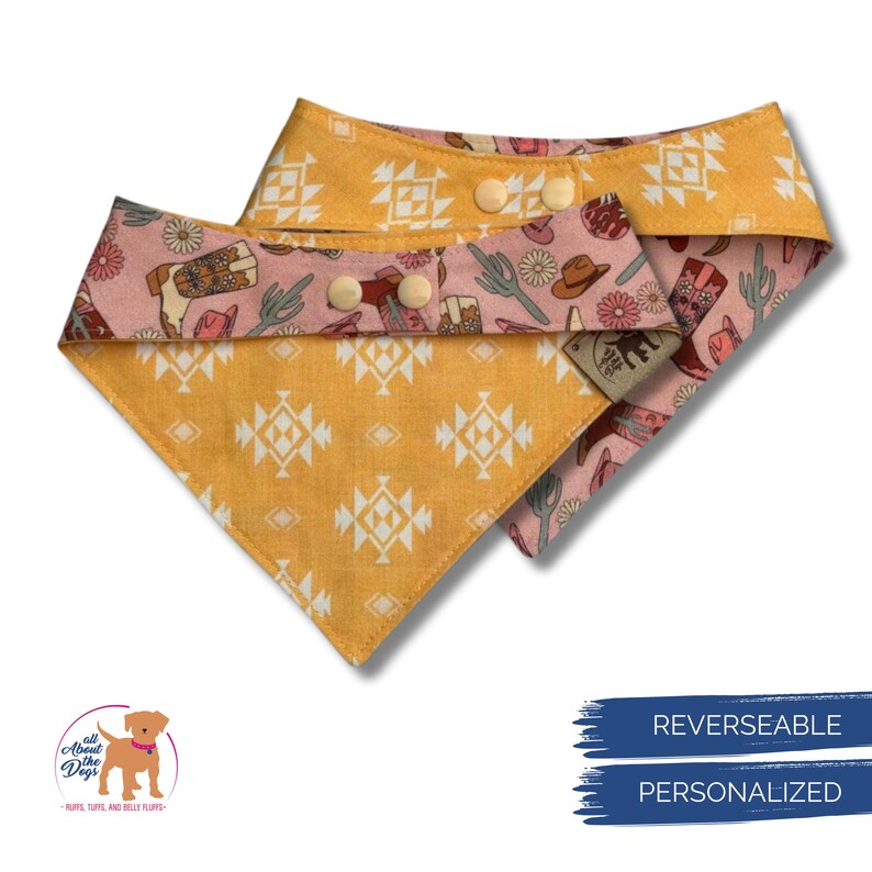 May include: Two reversible dog bandanas. One side is mustard yellow with a geometric pattern, the other is pink with a cowboy-themed print. The bandanas have snap closures and a small tag.