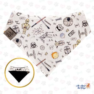 Op de afbeelding: Een witte bandana met een zwarte rand met een Star Wars-themaprint. De bandana heeft verschillende personages en objecten uit het Star Wars-universum, waaronder Darth Vader, R2-D2, C-3PO en de Millennium Falcon. De bandana bevat ook de tekst "Rule the Galaxy" en "Boom!" en "Kisssshhhh!"