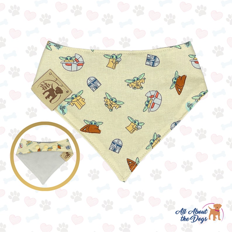 May include: A beige bandana with a repeating pattern of a green alien character, a spaceship, and a helmet. The bandana has a snap closure and is made of cotton.