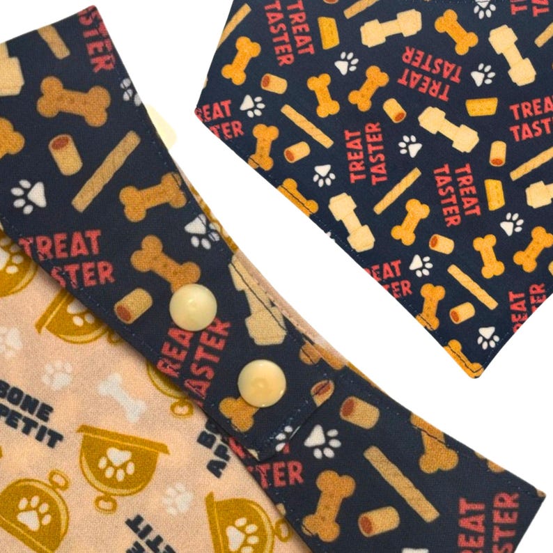 May include: Close-up of two dog bandanas. One is light tan with paw prints and the words "BONE PETIT". The other is navy blue with bone and treat graphics and the words "TREAT TASTER".