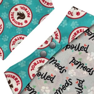 May include: Dog bandana with a teal background featuring white paw prints and red and white "Squirrel Patrol" circles. The bandana has gray snaps and a gray and white "Spoiled" print.