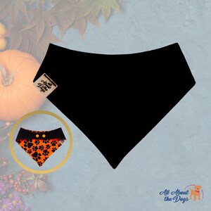 Peut inclure: Bandana noire pour chien avec une petite &eacute;tiquette &laquo; All About the Dogs &raquo;. Un encart montre un bandana orange et noir avec des empreintes de pattes et deux boutons jaunes. Le fond comprend une citrouille et des feuilles d'automne.