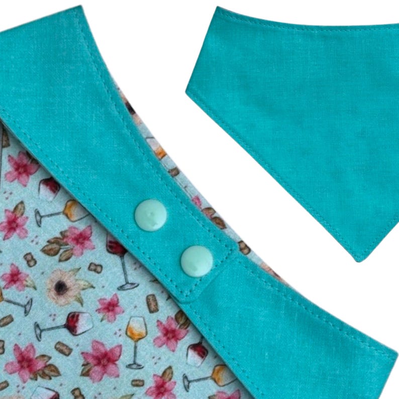 Pu&ograve; includere: Un bavaglino per bambini con finiture turchesi e chiusura a scatto. Il tessuto interno del bavaglino presenta un motivo floreale e bicchieri da vino. &Egrave; visibile anche una bandana turchese separata.