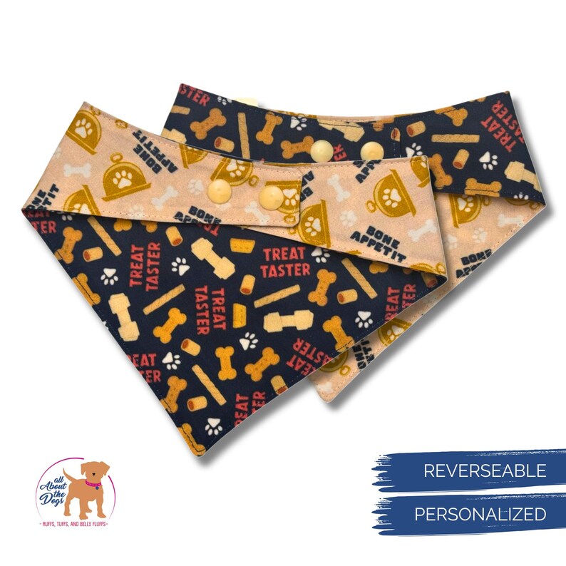 May include: Two reversible dog bandanas. One side features a navy blue background with bone and treat graphics, the other a tan background with a bone-shaped bowl graphic. The bandanas have snap closures and the words "Treat Taster" and "Bone Appetit".