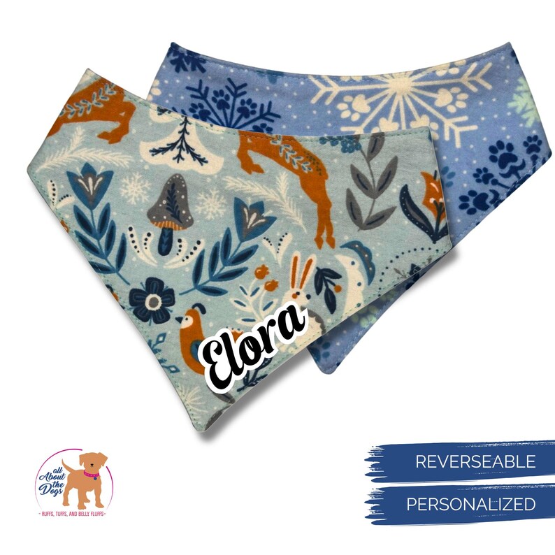 May include: Reversible and personalised dog bandana with a light blue floral pattern featuring deer, mushrooms, and rabbits. The name "Elora" is printed on the bandana. The reverse side has a blue snowflake pattern.