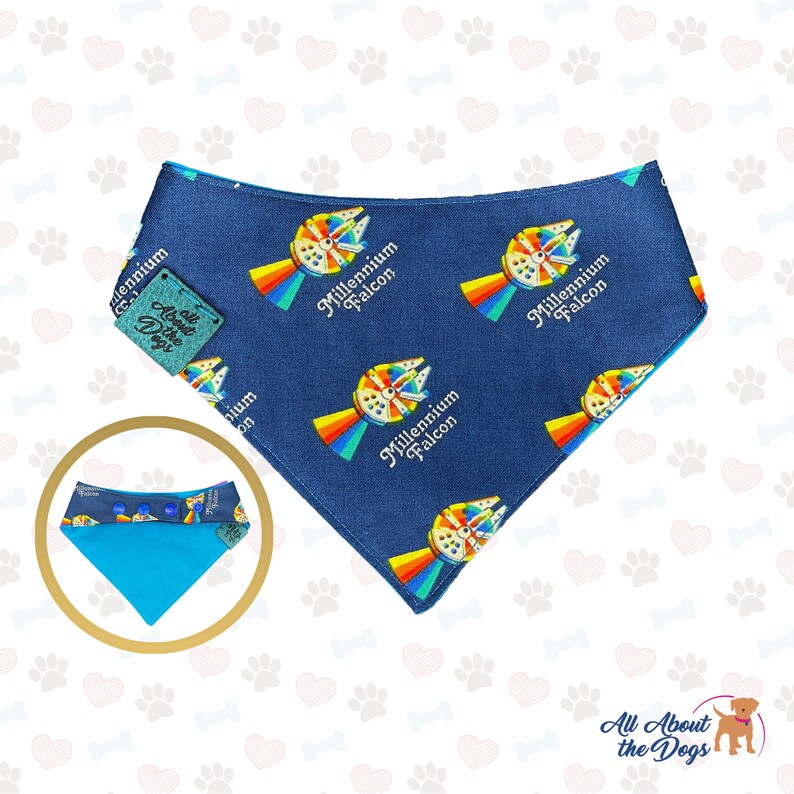 May include: Blue dog bandana with a repeating pattern of the Millennium Falcon spaceship with a rainbow behind it. The text "Millennium Falcon" is printed on each spaceship. The bandana has a blue and turquoise reversible side with snap buttons.
