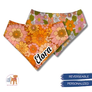 Puede incluir: Dos pa&ntilde;uelos reversibles y personalizados para perros. Uno es naranja con un estampado floral y el nombre "Elora" en blanco. El otro es blanco con un estampado floral. Los pa&ntilde;uelos son para mascotas.