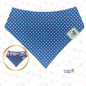 May include: A blue dog bandana with a polka dot pattern in pink and light blue. A smaller, reversible bandana with a floral pattern is shown in a gold circle. The tag reads "All About The Dogs".