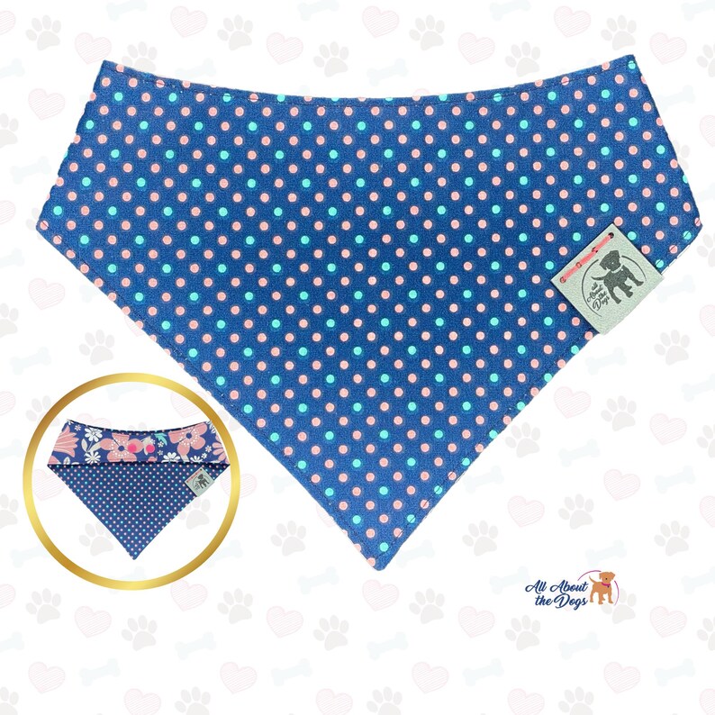 May include: A blue dog bandana with a polka dot pattern in pink and light blue. A smaller, reversible bandana with a floral pattern is shown in a gold circle. The tag reads "All About The Dogs".