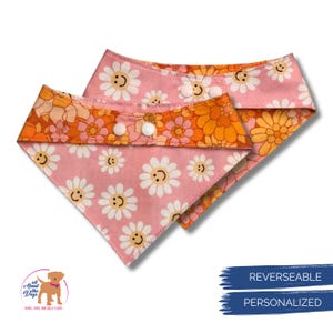 Puede incluir: Dos pa&ntilde;uelos reversibles para perros. Uno es rosa con caras de margaritas blancas, el otro es floral naranja y amarillo. Ambos pa&ntilde;uelos tienen cierres de bot&oacute;n a presi&oacute;n blancos. Los pa&ntilde;uelos son personalizados.
