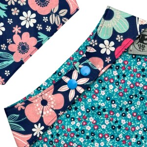 K&ouml;nnte beinhalten: Nahaufnahme eines floralen Stoffes mit marineblauem Hintergrund und rosa und wei&szlig;en Blumen. Der Stoff ist mit einem t&uuml;rkisfarbenen Blumenmuster und blauen bl&uuml;tenf&ouml;rmigen Kn&ouml;pfen versehen. Das Design ist eine Mischung aus gro&szlig;en und kleinen Blumenmustern.