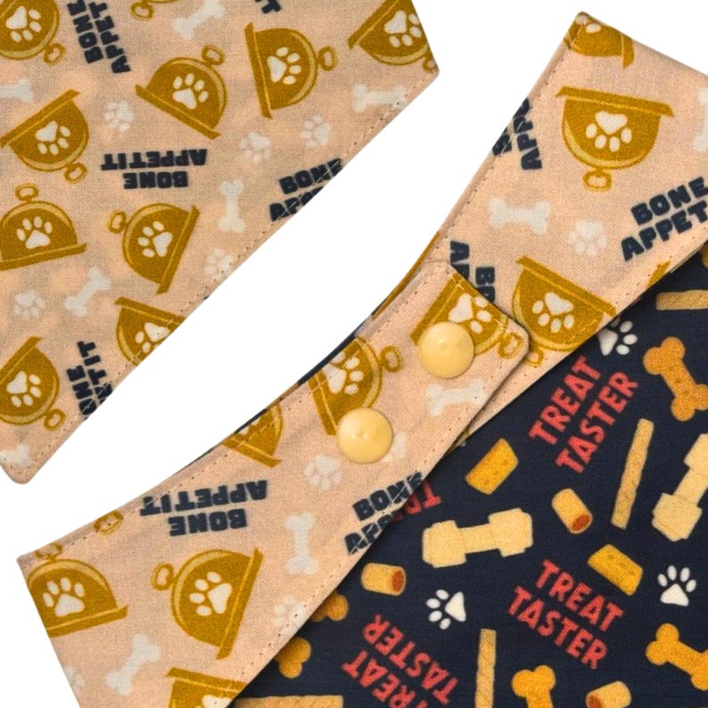 May include: Dog bandanas in tan and navy blue, featuring paw prints, bones, and the phrases "Bone Appetit" and "Treat Taster." The tan bandana has a gold trophy design. The navy blue bandana has a pattern of dog treats.
