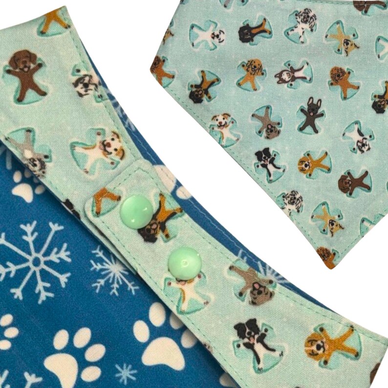 K&ouml;nnte beinhalten: Hunde-Bandana mit blau-wei&szlig;em Schneeflocken- und Pfotenmuster. Der Bandana hat einen hellblauen Besatz mit Hundeengel-Illustrationen und zwei gr&uuml;nen Kn&ouml;pfen zum Verschlie&szlig;en.